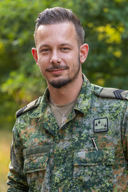 Portretfoto van sergeant Luc, achter hem bomen.