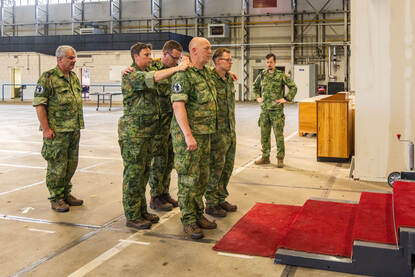 De draagploeg loopt met de lijkkist op een replica van de trap bij Paleis Noordeinde. Daarop ligt een rode loper. Daarnaast een viertal dat zich, met de armen over elkaar heen geslagen, naar boven verplaatst.’