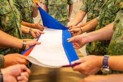 De acht militairen aan weerszijden van de kist vouwen de Nederlandse vlag tot een strak pakketje.