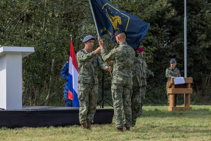 Generaal-majoor Johan van Deventer pakt de vlag van het nieuwe NLD JFC over van een marinier. Daarachter een klein podium met daarnaast een Nederlandse vlag.