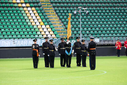 De vaandelwacht staat opgesteld in het stadion van ADO Den Haag. Daarvoor de commandant met een sabel in zijn hand.