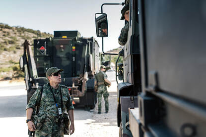 Een militair op de grond, praat met een militair in de cabine van een vrachtwagen.