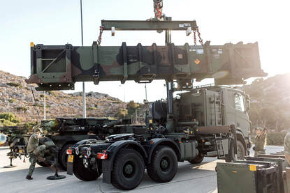 Een lanceerbuis van de Patriot hangt in de takels en wordt door militairen op de grond naar de juiste positie geleid.