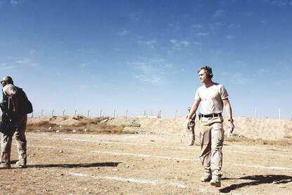 Kees loopt op een omheinde zandvlakte met oorkappen op.