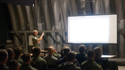 Twee militairen spreken een zaal vol mensen toe.