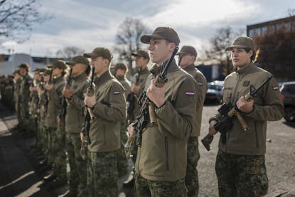 Rijen jonge mensen in groen defensietenue met geweer in de hand.