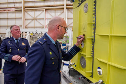 Een luchtmachtmilitair schrijft zijn naam op een grote gele metalen balk.