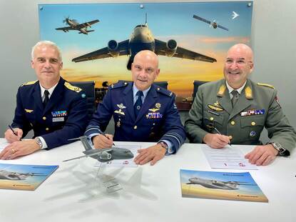 Drie militairen naast elkaar ondertekenen drie overeenkomsten.