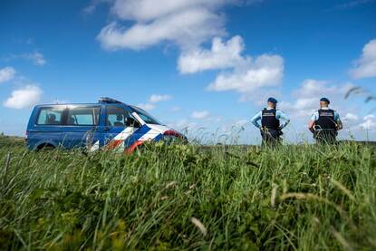 Twee marechaussees staan naast hun bus in een veld.