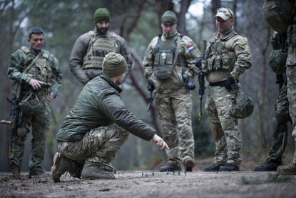 Een instructeur van het IMPT legt wat uit in het bos aan cursisten.