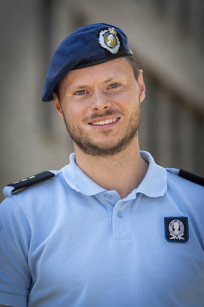 Portret van man met blauw KMar shirt en baret op die vriendelijk kijkt.