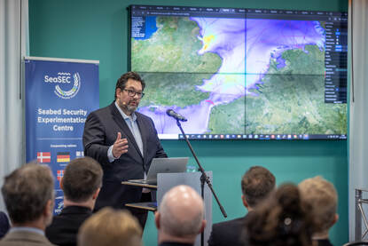 Sprekers geven een presentatie over de veiligheid van infrastructuur op de zeebodem voor een zaal met publiek.