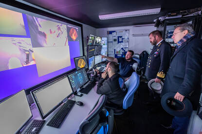 In een container bekijken mensen live beelden op verschillende schermen.