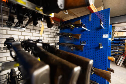 Doorkijkje over onscherpe geweren met op de achtergrond een rek met verschillende varianten AK-47.