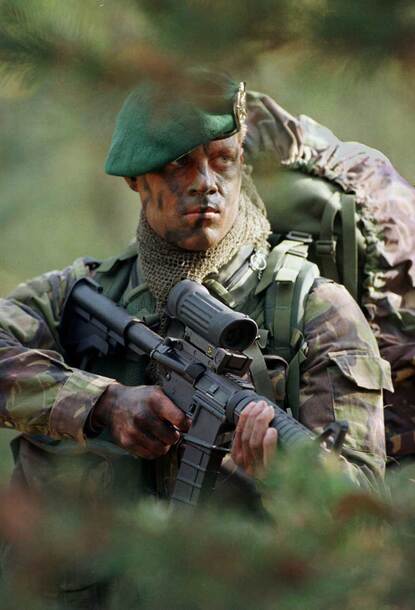 Nederlandse commando met groene baret en Diemaco C8 achter bladeren.