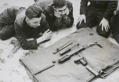 Landmachtmilitairen liggen voor een doek met daarop een gedemonteerde Uzi.