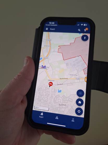 Een telefoonscherm waarop de applicatie te zien is. Een klein gebied op de landkaart is gemarkeerd met een rood vlak.