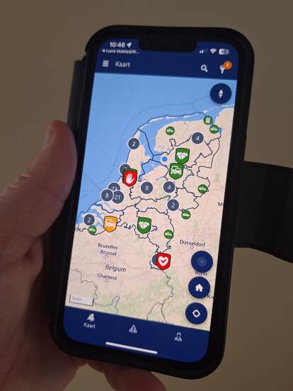 Een telefoonscherm waarop de applicatie te zien is. Op een kaart van Nederland staan icoontjes met daarop het type melding dat binnenkomt.