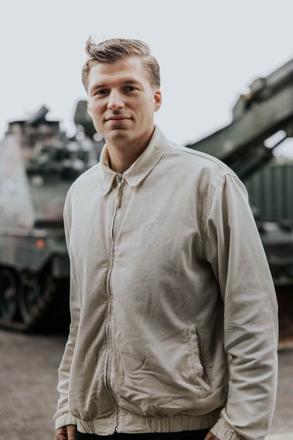 Daan kijkt in de camera. Hij draagt een witte jack. Achter hem is vaag de Kodiak te zien.