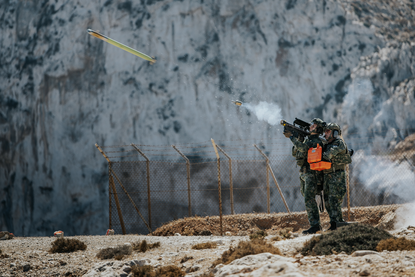 Een schutter schiet gesimuleerd met een Tracking Head Trainer op een F-16  van de Griekse luchtmacht op de NATO Missile Firing Installation (NAMFI). Foto ernaast: Een F-16 in de lucht.